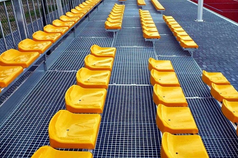trybuny stadionowe czterorzędowe z kratami pomostowymi wema i żółtymi nowoczesnymi krzesełkami 